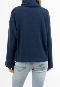 Pullover in pile blu navy con colletto alto, vestibilità comoda e maniche lunghe. Presenta una cucitura sul retro e dettagli di design sottili.