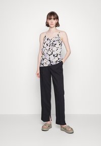 Camisola floral com alças finas, apresentando flores roxas e brancas sobre um fundo preto, combinada com calças pretas de perna reta e sandálias verdes.