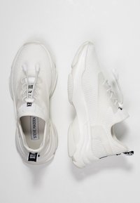 Paire de baskets blanches Steve Madden avec tissu en mesh, lacets élastiques sans nœud et semelles épaisses, montrées en vues de dessus et de côté sur fond blanc.