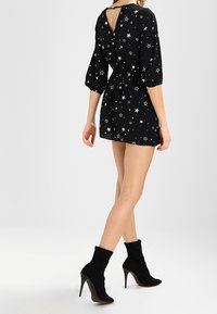 Vestido negro con estampado de estrellas, con cintura entallada, mangas abullonadas y espalda en V. Combinado con botas negras de tobillo. Textura suave.