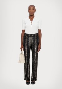 White ribbed short-sleeve top with lace-up detail, paired with black and gold sequined patterned trousers. Holding a small white handbag.