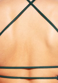 Mörkgröna tygband bildar ett korsmönster mot bar hud och framhäver en slät, jämn struktur utan extra dekoration.