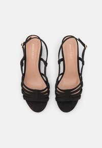 Sandali con tacco alto in suede nero, con cinturini incrociati multipli e una fibbia dorata, dotati di una soletta beige liscia.