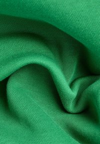 Tela de algodón verde, textura suave, tejido de punto ajustado, con sutiles variaciones en el tono y un ligero brillo, dispuesta en suaves pliegues.