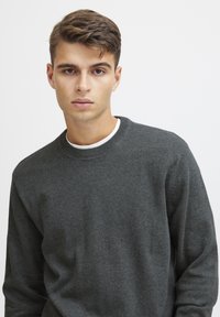 Suéter de punto gris oscuro con un cuello redondo acanalado y mangas largas. La tela parece suave y texturada, diseñada para un ajuste ceñido.