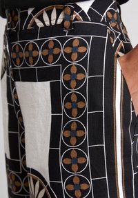 Pantaloni in tessuto nero con un motivo geometrico a contorni bianchi, motivi floreali marroni e blu, e una finitura testurizzata.