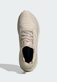 Light beige athletic shoe with a textured upper, reinforced toe cap, laces, and a black insole featuring "ULTRABOOST" printed.