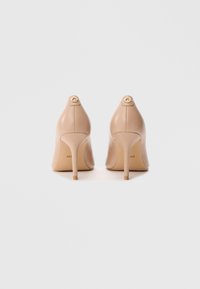 Scarpe con tacco alto in pelle beige con punte appuntite, sottili tacchi a spillo e dettagli con emblema G dorato sul retro. Texture liscia.