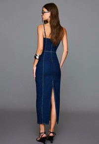 Abito lungo in denim con spalline sottili, design aderente e uno spacco posteriore, caratterizzato da cuciture a contrasto e una superficie liscia.