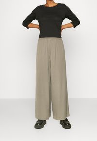 Black, fitted long-sleeve top paired with light gray, wide-leg pants. Pants have an elastic waistband; model wears black platform shoes.