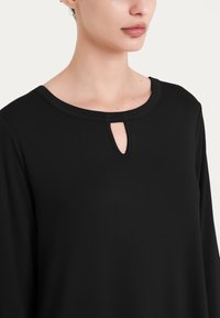 Maglietta nera a maniche lunghe con scollatura rotonda e dettaglio a chiave. Realizzata in tessuto morbido con una consistenza liscia. Design semplice.