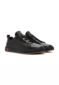 Zapatillas negras de cuero con una textura suave, punta redondeada, costuras elevadas y acentos marrones en el talón y la suela.