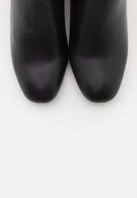 Botas de tobillo de cuero negro con una textura suave, punta redondeada y un diseño elegante. Estilo minimalista sin hardware ni acentos visibles.