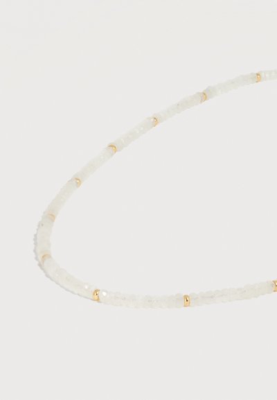 Κολιέ με μικρές, στρογγυλές λευκές χάντρες που εναλλάσσονται με μικρές χρυσές ενδιάμεσες χάντρες, τοποθετημένο σε απαλή καμπύλη σε λευκό φόντο.