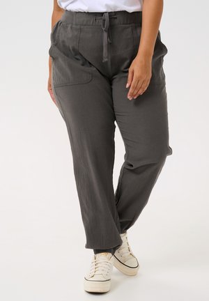 Pantalones grises, ligeros y de corte relajado, con cintura elástica y bolsillos laterales, combinados con zapatillas blancas y una camiseta casual.