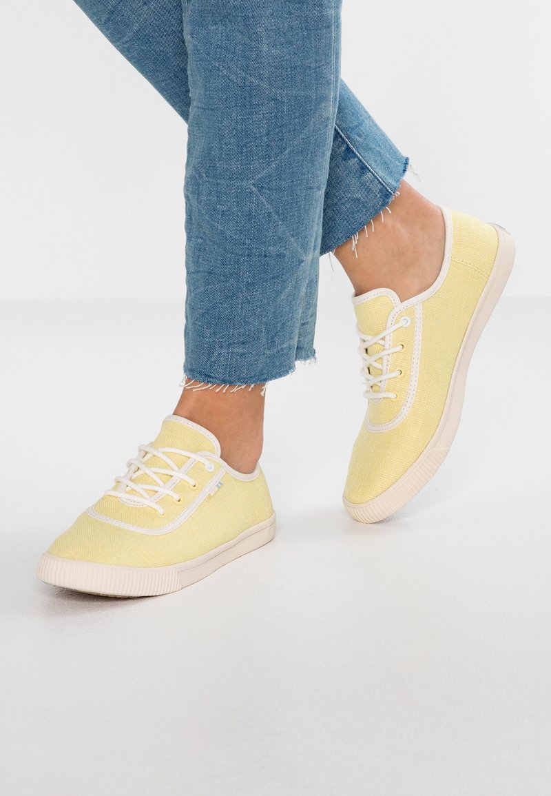 Baskets en toile jaunes avec une finition texturée, accents blancs et lacets. La semelle en caoutchouc est beige avec des détails striés.