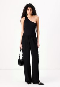 Haut noir à épaule dénudée en tissu côtelé, associé à un pantalon noir ample doté d'une taille élastique, et des ballerines noires à bout pointu.