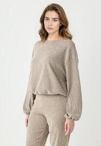 Ensemble bi-matière en tricot beige texturé composé d'un haut ample à manches longues et ballons, accompagné de pantalons ajustés assortis.