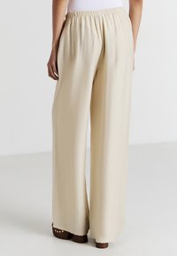 Pantalons beige à jambes larges en tissu doux avec une taille élastique. Présente une texture lisse et une coupe décontractée.