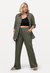 Ensemble en lin vert olive comprenant une chemise et un pantalon. La chemise possède des boutons et des manches retroussées ; le pantalon a une taille avec cordon de serrage et des poches latérales.