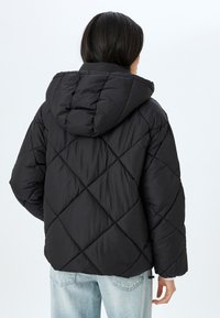 Sort quilted dunjakke med hætte, med et diamantmønster og en afslappet pasform. Blød tekstur, dobbelt sidelommer og justerbar kant.