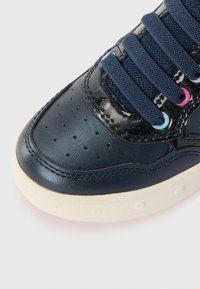 Sneaker in pelle navy con punta perforata, dettagli in patent strutturato, lacci scuri e suola in gomma chiara con dettagli circolari.
