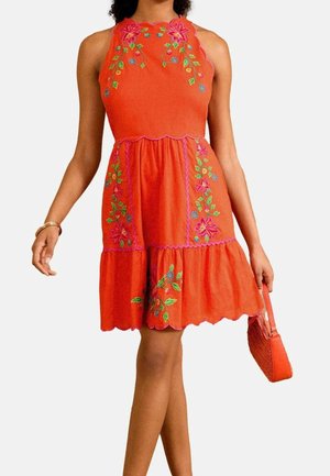 Ärmelloses orangenes Kleid mit Blumenstickerei, wellenförmigen Kanten und einem gerafften Rock, getragen mit einer passenden orangen Handtasche und goldenem Armband.