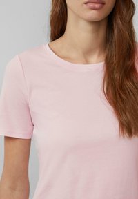 Lichtroze T-shirt met korte mouwen en een ronde hals, gemaakt van zachte stof, met een gladde textuur en minimale stikdetails.