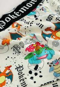 Bomulds shorts med levende Pokémon designs i orange, blå og grøn. Sort talje med "Pokémon" tekst. Mønstret inkluderer karakterillustrationer.