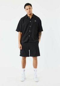 Zwarte gestreepte korte mouwen overhemd met kraag, gecombineerd met bijpassende korte broek. Heeft witte accenten en knopen, gedragen met witte sneakers.