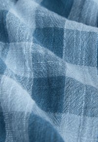 Gros plan sur un tissu à carreaux bleu et blanc doux avec un tissage texturé et des plis doux.