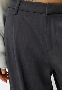 Pantaloni grigio scuro in tessuto testurizzato con vestibilità su misura, caratterizzati da una vita piatta e tasche laterali. Aspetto casual abbinato a un top grigio chiaro.