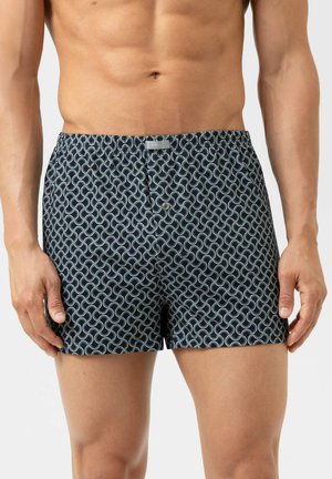 Männlicher Oberkörper in schwarzen Boxer-Shorts mit einem verschlungenen weißen Kreis-Muster und einem vorderen Knöpfverschluss.