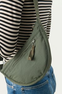 Borsa a tracolla verde a forma semisferica realizzata in tessuto con superficie testurizzata, dotata di zip e un accento di nappina in tessuto.