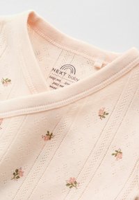 Ljusrosa babywrap-top med små blommönster och delikata hålsömstripes, med en mjuk ribbad halsringning.