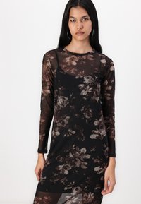 Robe noire à manches longues en tissu transparent, ornée d'un motif floral dans des nuances de brun et de gris, avec une coupe décontractée et un col rond.