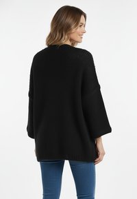 Czarny dziany sweter o luźnym kroju, z opuszczonymi ramionami i rękawami długości 3/4. Tkany wzór, dół swetra sięga poniżej bioder.