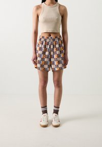 Top corto color beige, shorts sueltos con estampado geométrico en amarillo, azul y naranja, zapatillas blancas y calcetines marrones a rayas.