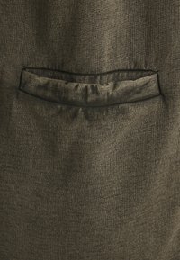 Tessuto di un verde oliva scuro con texture visibile, caratterizzato da tasca e bordi arricciati lungo l'apertura e una finitura complessiva liscia.