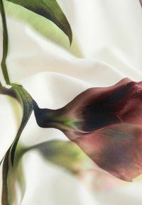 Gros plan d'un tissu crème avec un motif floral abstrait doux en tons verts, bruns et bordeaux, montrant la texture et des plis légers.