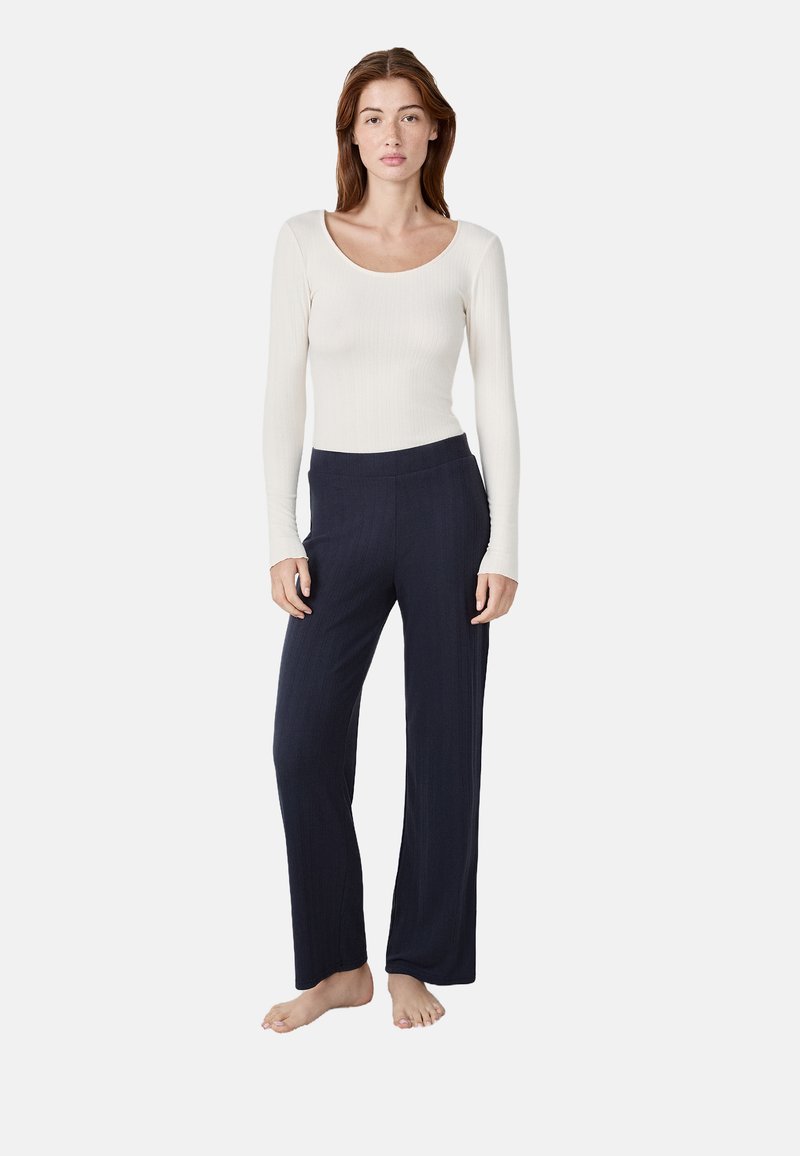 Top a maniche lunghe a costine in crema abbinato a pantaloni a gamba larga blu scuro, con una texture liscia e una vita aderente.