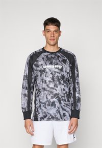Das langärmlige Sporttrikot verfügt über ein schwarzes und graues digitales Tarnmuster, hat einen runden Ausschnitt und ein gesticktes "UMBRO"-Logo auf der Brust.