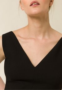 Svart klänning med V-ringning, utan ärmar och en figurnära silhuett. Slät textur med rena linjer och minimal detaljer.