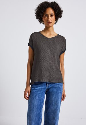Haut à manches courtes et col en V de couleur gris foncé avec un motif géométrique, en tissu doux ; associé à un jean large bleu clair.
