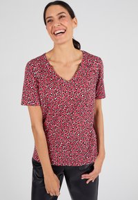 Camiseta de manga corta roja con escote en V, que presenta un estampado de leopardo en blanco y negro, hecha de una tela suave y ligera.