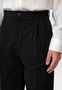 Zwarte broek met streepjes en geplooide voorkant, voorzien van een knoopsluiting en ceintuurlussen, gemaakt van gladde stof met een getailleerde pasvorm.