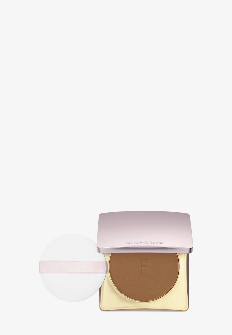 Bronzer prasowany w różowo-złotym opakowaniu, zawierający okrągły biały aplikator z różowym paskiem, gładką powierzchnię i matowe wykończenie.