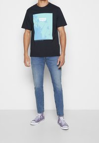 Černé tričko s světlemodrým grafickým motivem palem a nápisem "Levi's", doplněné světlemodrými džínami a fialovými teniskami.