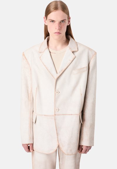 Hellbeige Oversized-Blazer mit strukturiertem Finish, kontrastierenden Nähten, zwei Knöpfen und einer Brusttasche. Getragen über einem gerippten Oberteil.