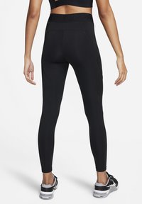 Kobieta ubrana w czarne legginsy Nike Pro z wysokim stanem i czarno-białe buty sportowe, pokazana z tyłu na białym tle.